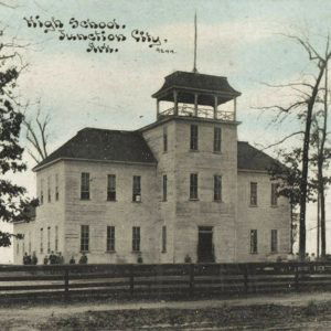 Multistory white wooden building with cupola on top and people standing around on the ground