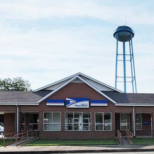 Single story red brick post office building with water tower in background