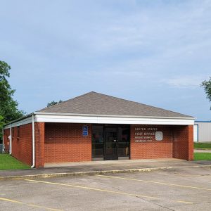 Single story red brick post office building with parking lot