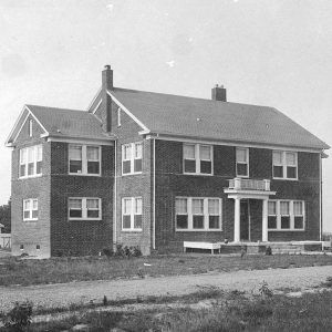 Multistory brick building with white wooden small building in the background