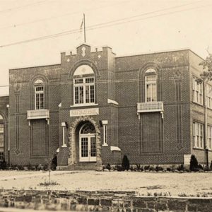 Multistory brick building with flag on pole on roof and arched front entrance