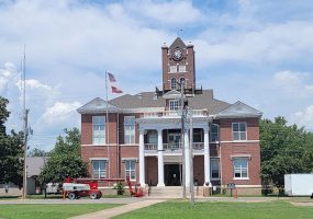 Multistory red brick building with clock tower and white columns with construction equipment in front