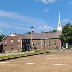 Multistory red brick church building with large tree out front