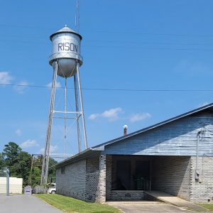 Cylindrical metal tank atop tall metal legs with "Rison" printed on it