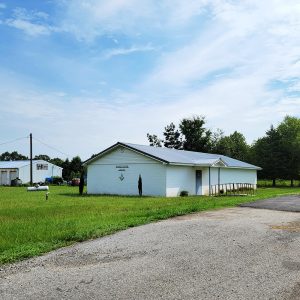 Single story white concrete block building next to road next to another white building