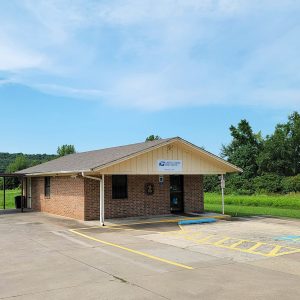 Single story red brick post office building with sign saying "Romance" and parking lot