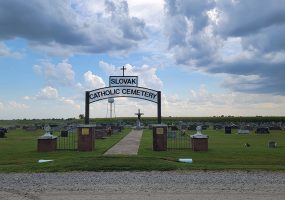 Cemetery with grass and gravestones and arched sign reading "Slovak Catholic Cemetery"