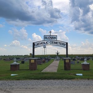 Cemetery with grass and gravestones and arched sign reading "Slovak Catholic Cemetery"