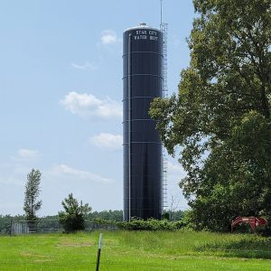 Large black cylindrical tower in the middle of a field with "Star City Water Department" on it in white letters