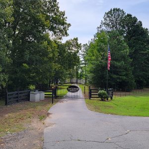 Barely visible single story building behind gate with sign "The Lodge at Romance" and trees on either side of gate