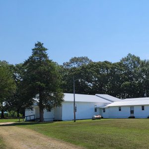 single-story white wooden church buildings amid trees