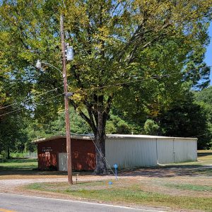 Single story white and red metal church building beneath trees