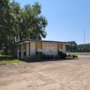 Single story small white and yellow metal building with awnings over windows and a parking lot