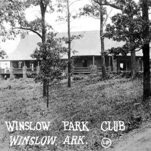 Multistory rock building with extensive porch behind some trees