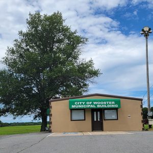 Single story tan block building with green and white sign reading "City of Wooster Municipal Building"