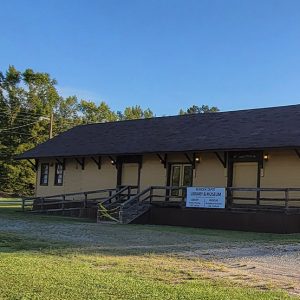 Single story yellow wooden building with porch and brown roof