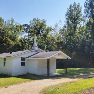 Single story white concrete block church building with steeple and covered entrance