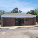 Single story red brick building with glass front door and parking lot