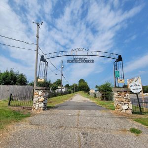 Small road through arched iron gate with lettering "Rockport Cemetery"