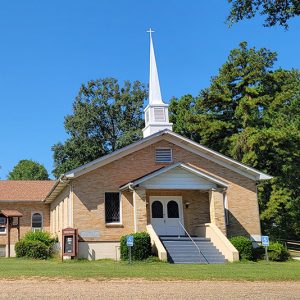 Multistory tan brick church building with covered entrance and steeple