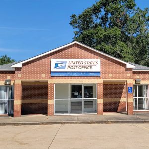 Single story red brick post office building with parking lot