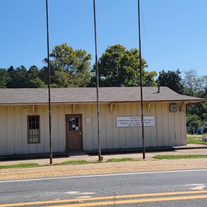 Single story tan wooden building with three poles in front