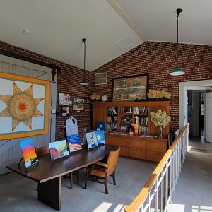 Room full of museum displays such as a quilt and a bookcase with books