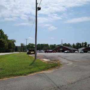 Red brick church building with white steeple and cars in parking lot