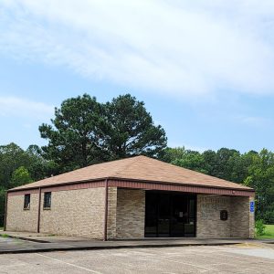 Single story tan brick building with parking lot and flagpole