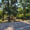 Single story tan aluminum siding building with blue sign in front and trees