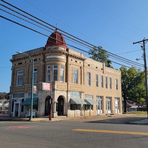 Street corner with multistory tan brick building with red dome on top