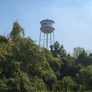 white metal water tank on tall legs with trees in foreground