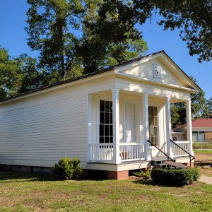 Single-story off-white wooden building with covered front porch and star detail above