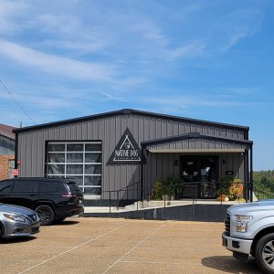 Single story black metal building with parking lot and triangular sign saying "Native Dog Brewing"