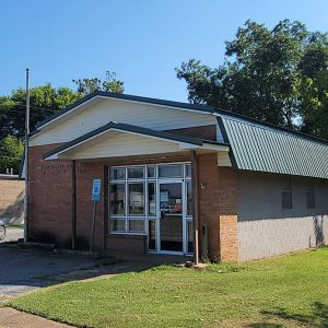 Small single story orange brick post office building with parking lot