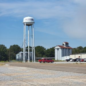 white metal water tower on legs with "Palestine" on the side next to round silver metal silos