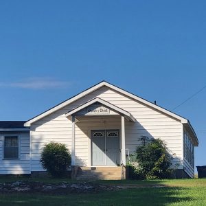 Single story white wooden church building with stairs leading to covered entrance