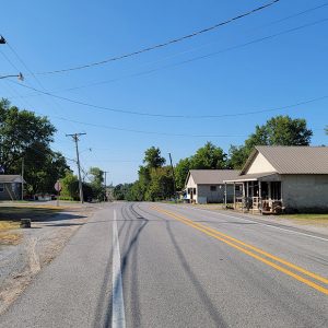 Road with single story buildings on either side and trees in background