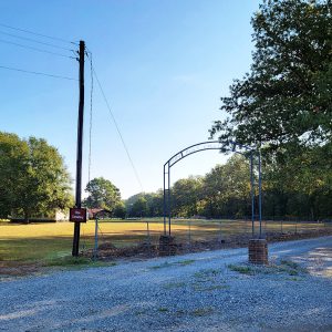 Metal arch and gate leading to cemetery and a small building behind trees