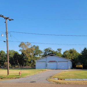 white metal building with with three bay doors and a yellow truck next to it