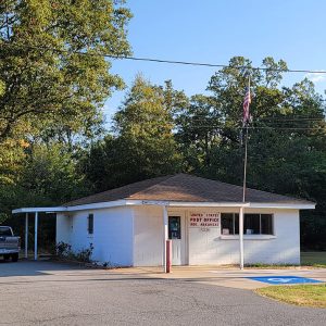 Single story white concrete block building with a pickup truck next to it and parking lot