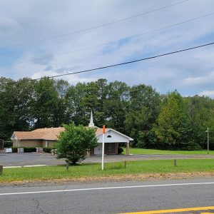 Multistory tan brick church building with steeple and parking lot