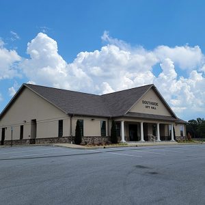 Beige wooden building with covered entrance and small white pillars and parking lot