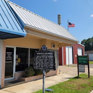 Single story yellow metal building with Sparkman historical sign out front