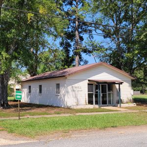 Single story white brick library building with trees around it