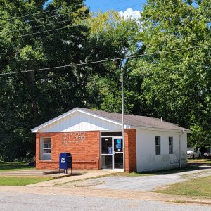 Single story post office building with red brick front and trees in background