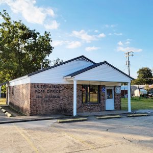 small brick building with white siding and covered entrance and parking lot