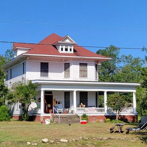 Multistory white wooden house with red roof and porch on first floor