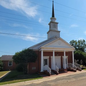 Multistory red brick and white wood church building with white columns in front and steeple