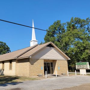 Single story tan brick church building with steeple